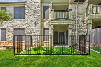 A black iron fence surrounds a green lawn in front of a stone building.